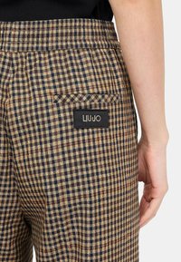 Pantaloni a quadri marroni e blu con tasca posteriore e un'etichetta nera con la scritta "LIU JO". Il tessuto ha una consistenza liscia e un design su misura.
