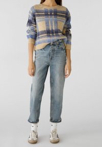 Pull en tricot à carreaux beige, bleu et bleu foncé ; jean taille haute bleu clair ; chaussettes blanches montant jusqu'à la cheville ; baskets gris et beige.