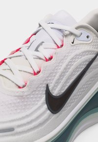 Λευκό αθλητικό παπούτσι Nike με μαύρο λογότυπο swoosh, υφασμένο επάνω μέρος, λευκά κορδόνια και εμφανές αεριζόμενο πέλμα σε αποχρώσεις τιρκουάζ και λευκού.