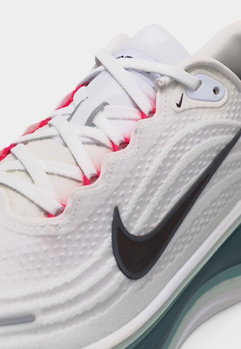 Biała sportowa Nike z czarnym logo w kształcie łyżwy, teksturowaną cholewką, białymi sznurowadłami i widoczną podeszwą z poduszką powietrzną w kolorach szmaragdu i bieli.