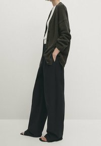 Ylimitoitettu tummanvihreä neuletakki, kevyt neulos, avoin etuosa. Yhdistetty korkeavyötäröisiin mustiin leveälahkeisiin housuihin ja tasapohjaisiin sandaaleihin.