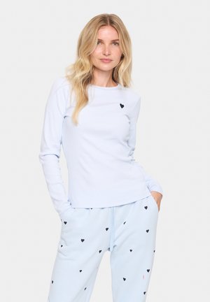 Lichtblauwe top met lange mouwen en een ronde halslijn, voorzien van een klein zwart hartdetail op de borst, gecombineerd met lichtblauwe broek met zwarte hartpatronen.