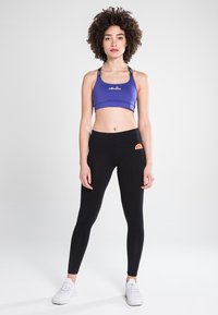 Lilla sports-bh med logo, sorte leggings med fargekontrast logo-lapp, glatt stoff, tettsittende design, brukt med hvite joggesko.