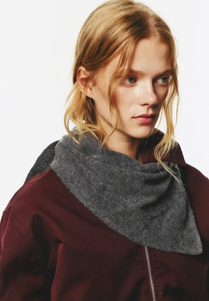 Grau Wollschal, der um den Hals drapiert ist, mit einer weichen Textur und ungleichmäßigem Saum, kombiniert mit einer kastanienbraunen Jacke.