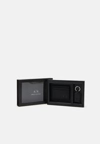 Schwarze Lederbörse mit Kartenfächern, Schlüsselanhänger und geprägt "A/X"-Logo, präsentiert in einer eleganten schwarzen Box mit einem transparenten Deckel.