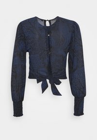 Navyblaue Bluse mit langen Ärmeln, strukturiertem Stoff, vorderer Bindeschleife und Knopfverschluss auf der Rückseite. Besitzt ein dezentes Muster.