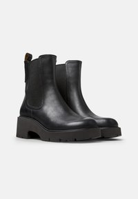 Mustat nahka ankle-boots, joissa on joustavat sivupaneelit, pyöreä varvas, paksu pohja ja vetotakki takana helppoa pukemista varten.