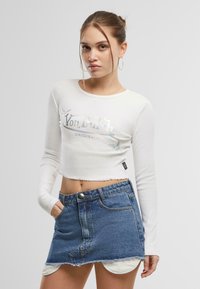 Vit långärmad croppad topp med iriserande "Von Dutch" grafik och blå denimkort kjol med fransad nederkant och framfickor.
