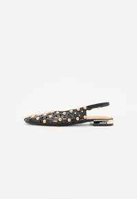 Scarpa slingback nera con design intrecciato, decorata con borchie metalliche, tacco flat e un accento dorato lucido sul tacco.