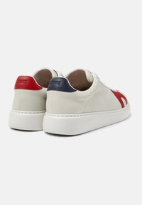 Un paio di sneakers bianche con suole spesse, dettagli rossi e blu navy sul tallone e un design rosso sul lato esterno, mostrati da un'angolazione posteriore.