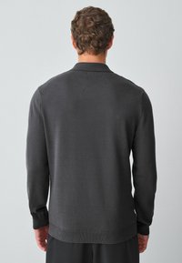 Sötétszürke kötött pulóver gallérral, hosszú ujjakkal és bordázott mandzsettával. Simaszerkezetű, letisztult, minimalista dizájn.