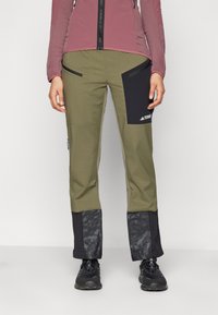 Pantalons de plein air pour hommes en vert olive avec des accents noirs, poches zippées et panneaux inférieurs texturés. Fabriqués en matériau durable et résistant aux intempéries.