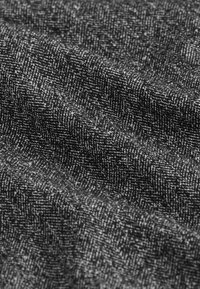 Sort-hvidt stof med et struktureret sildebensmønster, vist i nærbillede med synlige fibre og bløde folder.