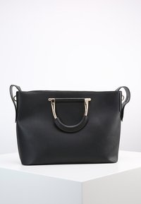 Svart läderhandväska med rektangulär form, guldfärgad hårdvara och dubbelhandtagsdesign. Har ett dragkedjefack upptill och justerbar axelrem.