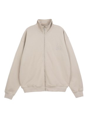 Beżowa bluza zapinana na zamek z wysokim kołnierzem, długimi rękawami, ściągaczami na mankietach oraz napisem "Varsity Champion" na lewej piersi.