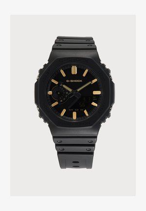 Montre G-Shock noire avec index et aiguilles dorés, sous-affichage numérique et bracelet en résine noire résistante.