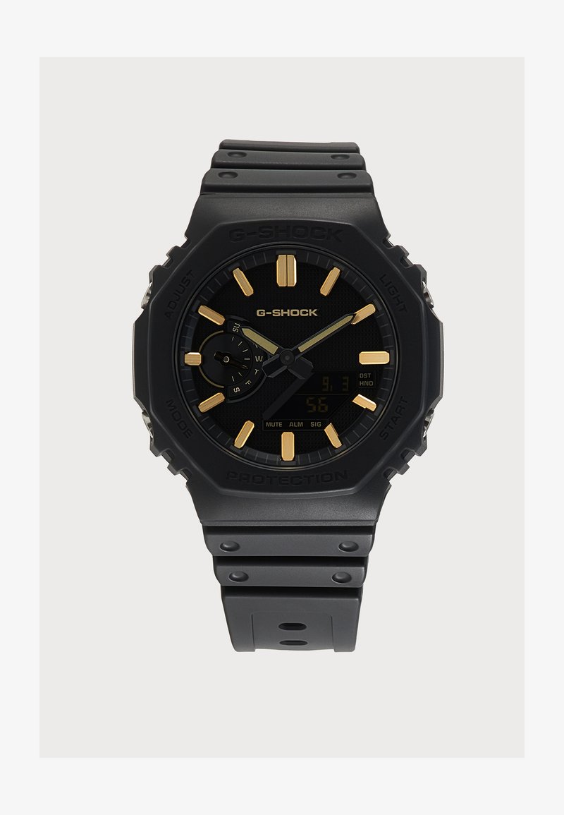 Μαύρο ρολόι G-Shock με χρυσά στοιχεία ωρών και δείκτες, ψηφιακή υπο-οθόνη και ανθεκτικό μαύρο λουρί από ρητίνη.
