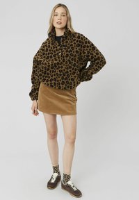 Pull en polaire à imprimé léopard brun et noir, col montant, associé à une mini-jupe en velours côtelé beige et des chaussettes à imprimé léopard. Baskets marron.