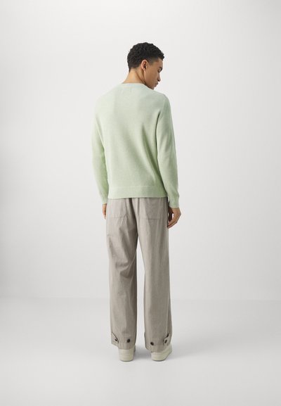 Lys grønn ribbestrikket genser med avslappet passform, kombinert med beige vide bukser med sidestolper. Myk tekstur; minimalistisk design.
