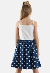 Robe à pois bleus avec un haut blanc et des bretelles fines. La jupe est froncée, avec de grands pois blancs sur un fond marine.