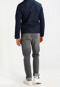 Marinblå jacka med krage, i kombination med ljusgrå jeans med uppvikta ärmar och vita sneakers. Enkel design, avslappnad passform.