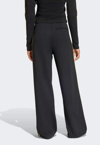 Svarta vida byxor med en slät tygtextur, med gula sidostrek och en enda bakficka för detalj.