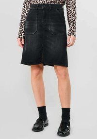 Zwarte denim rok met twee voorzakken, een rechte snit, ruwe rand en subtiele vervaging. Gecombineerd met zwarte sokken en loafers.