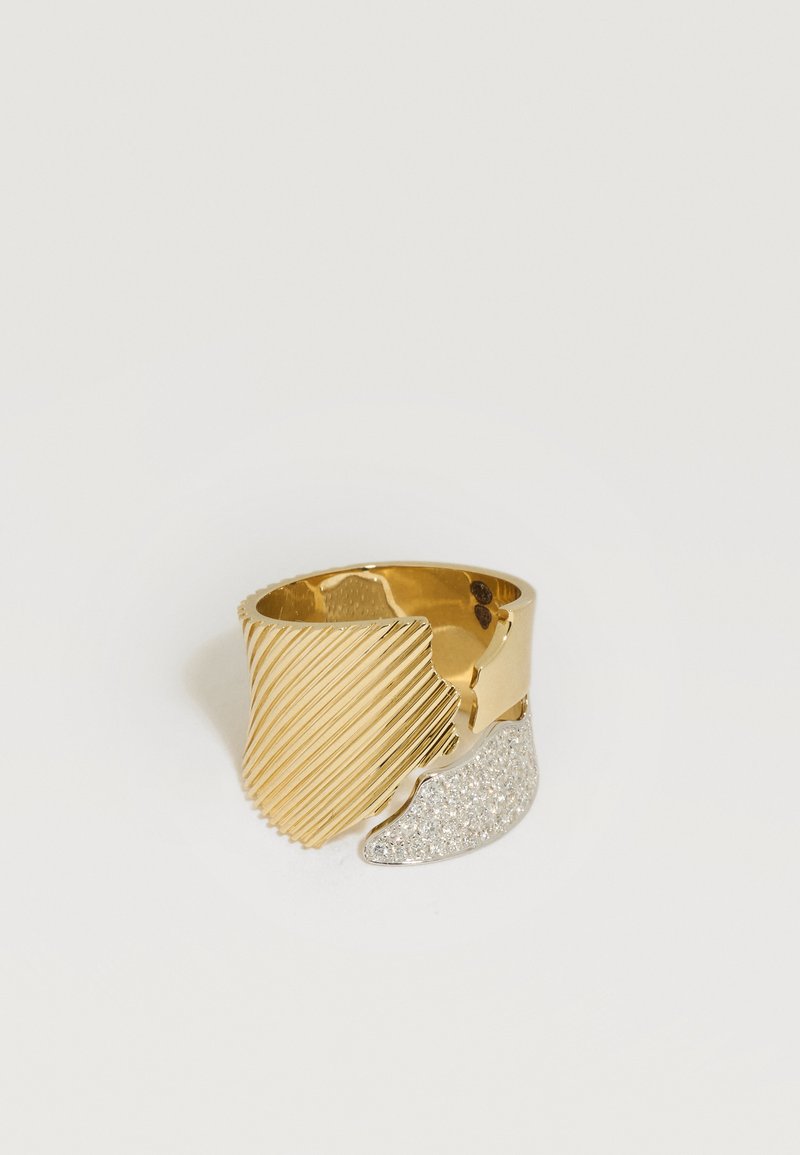 Bague à large bande en tons or et argent avec des rainures diagonales sur le côté or et un côté argenté texturé pailleté sur fond blanc.