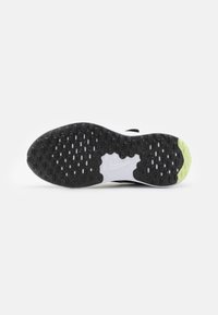 Semelle de chaussure de sport en noir et blanc avec du caoutchouc texturé, présentant un motif unique et des accents verts au niveau du talon.