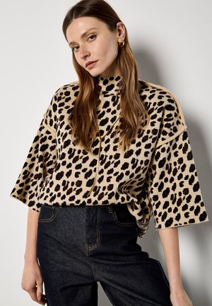 Leopardenmuster-Pullover in Beige und Schwarz, mit hohem Kragen und weiten Ärmeln, kombiniert mit dunklen Jeans. Weiche Textur.