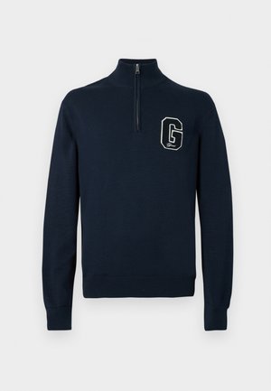 Námornícky modrý pulóver s dlhými rukávmi a polovičným zipsom na golieri, s bielou nášivkou „G“ na ľavej hrudi.