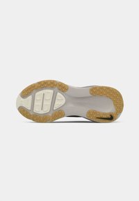 Semelle de chaussure avec des pads en caoutchouc beige antidérapants et des segments de coussinage blancs, avec un petit logo noir sur la zone du talon.