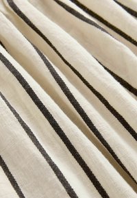 Tejido de lino con una base de color crema claro y franjas verticales oscuras. Suave textura, fibras naturales y un ligero brillo crean un interés visual.