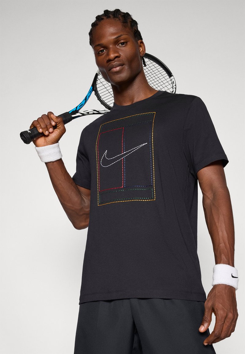 Zwarte Nike t-shirt met korte mouwen, voorzien van een meerkleurig geborduurd vierkant ontwerp en logo. Het model houdt een tennisracket vast en draagt polsbanden.