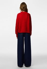 Red knitted sweater with a cropped design, paired with high-waisted, wide-legged dark denim jeans. Smooth texture and relaxed fit.