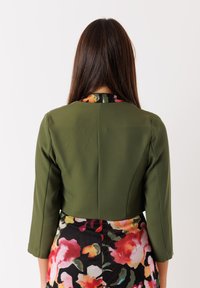 Giacca verde corta con maniche a tre quarti; presenta un motivo floreale sul colletto e una texture liscia.
