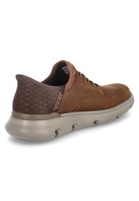 Sneaker in pelle marrone con tacco strutturato di un marrone scuro, suola in gomma beige e design con lacci. Presenta un collare imbottito e un discreto dettaglio del logo.