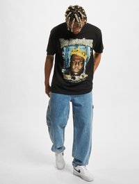 Black cotton t-shirt features a graphic print of a crowned face, with "The Notorious" text; paired with light blue baggy jeans and white sneakers.