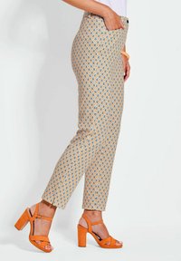 Pantaloni a fantasia con motivo a rombi gialli e blu, dalla vestibilità slim. Abbinati a sandali con tacco blocco arancioni, che presentano un design a strap.