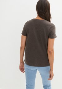 T-shirt marrone a maniche corte con scollatura rotonda, texture morbida e vestibilità rilassata, abbinato a jeans azzurri chiari.