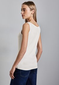 Top blanco sin mangas con un escote redondo, forma ajustada y textura suave, combinado con pantalones de pierna ancha de color azul oscuro.