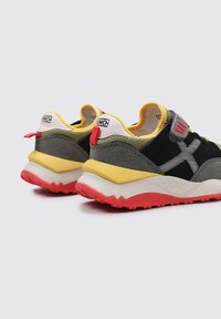 Zapatillas deportivas con parte superior en gris y negro, acentos en amarillo y rojo, tejido texturizado y una suela gruesa en blanco y rojo.