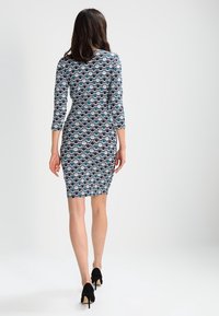 Sukienka bodycon w wielokolorowym okrągłym wzorze na ciemnym tle, z rękawami o długości trzech czwartek i długości do kolan, w połączeniu z czarnymi szpilkami.