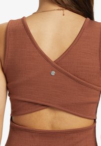 Brun tekstureret crop top med V-rygdesign, der har krydsede stropper og en lille sølvknapdetalje på ryggen.