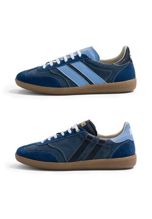 Deux baskets basses décontractées en daim bleu foncé et bleu clair avec des lacets blancs et des semelles en caoutchouc marron, vues de profil.