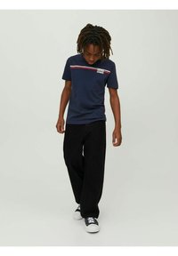 Marinblå bomullströja med röda och vita horisontella ränder och tryckt logotyp på bröstet, kombinerad med svarta vida byxor och sneakers.