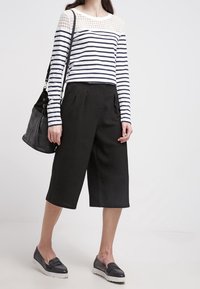 Randig långärmad topp med spetsdetalj, i kombination med svarta culottes. Svart handväska och strukturerade slip-on skor fulländar looken.