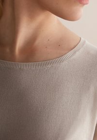 Lys taupe striktrøje med bred halsudskæring og fine ribbede detaljer. Stoffet fremstår glat med en subtil glans og tekstur.