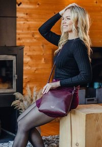 Kabelka přes rameno z burgundské kůže s nastavitelným popruhem, hladkou texturou, minimalistickým designem a logem na přední straně.