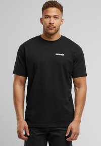 Sort bomulds T-shirt med rund hals og korte ærmer, forsynet med et lille hvidt "DEFSHOP" logo på venstre bryst.